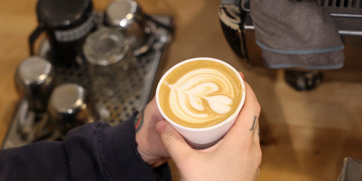 A small coffee shop owner looking concerned while standing behind a counter with coffee equipment.