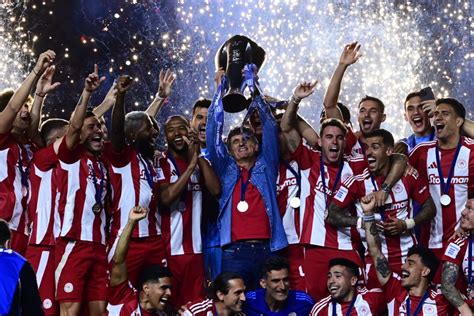 Olympiacos players lifting the championship trophy amidst celebrating fans.
